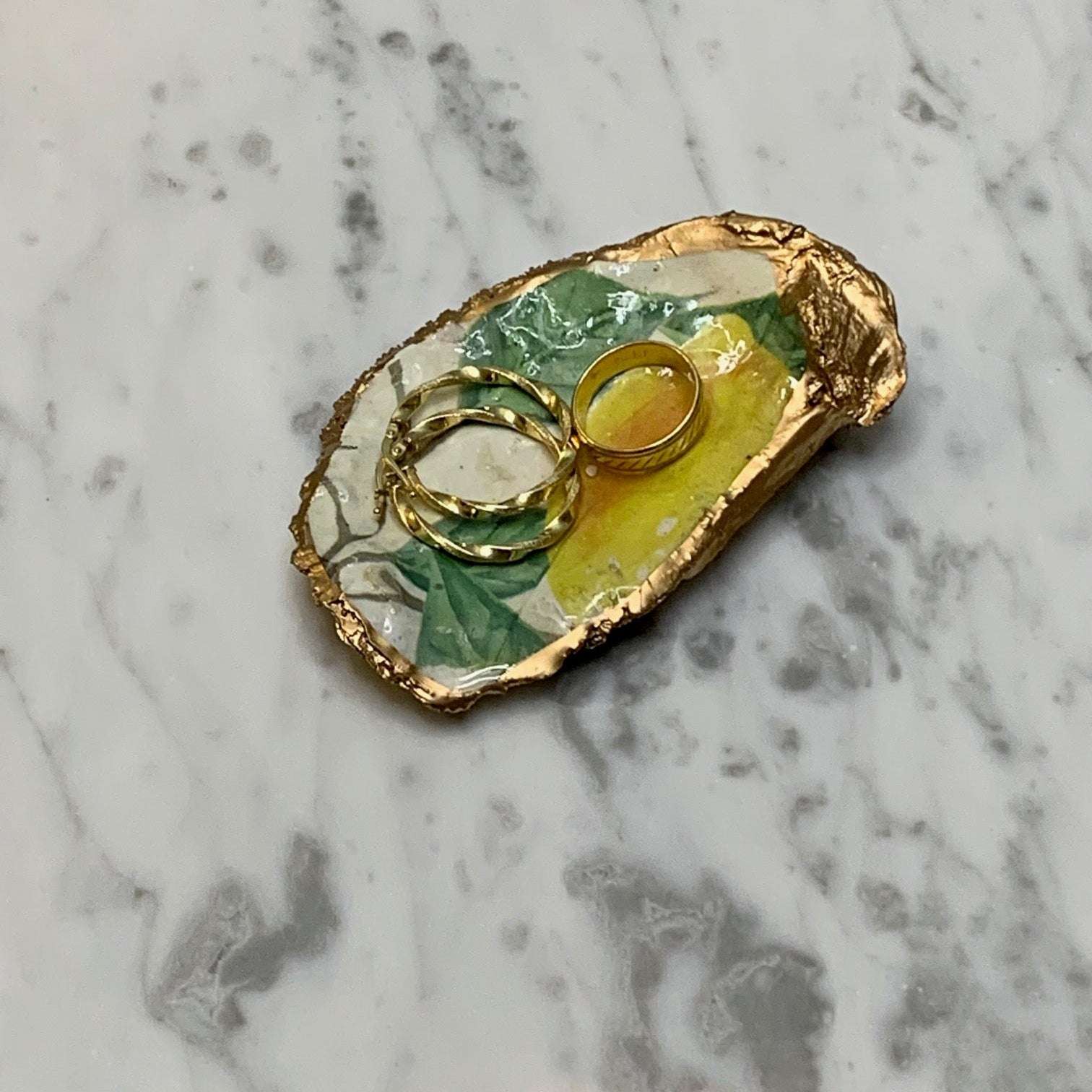Unique oyster shell jewelry dish with hand-painted lemons and gold trim, offering a touch of coastal elegance to any dresser or vanity