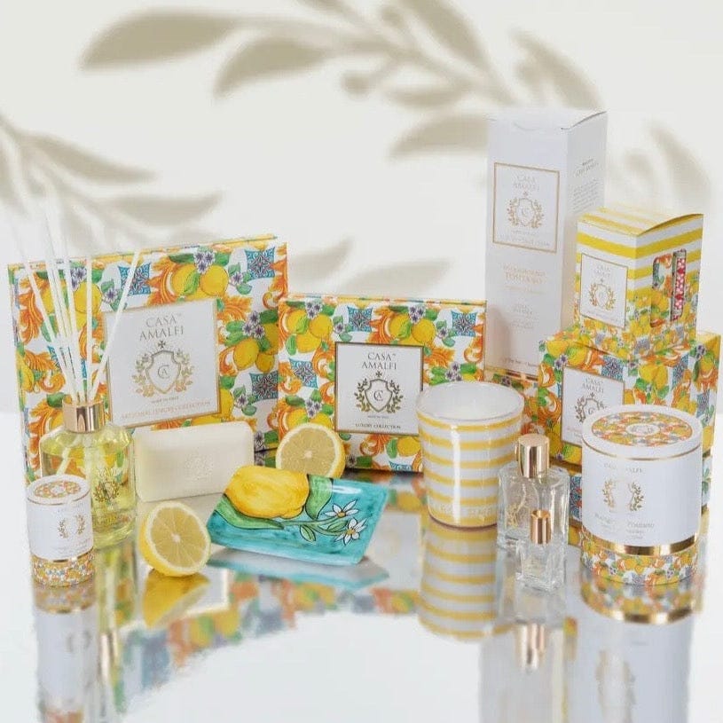 Casa Amalfi home decor and fragrance set with lemon-themed packaging on a reflective surface.